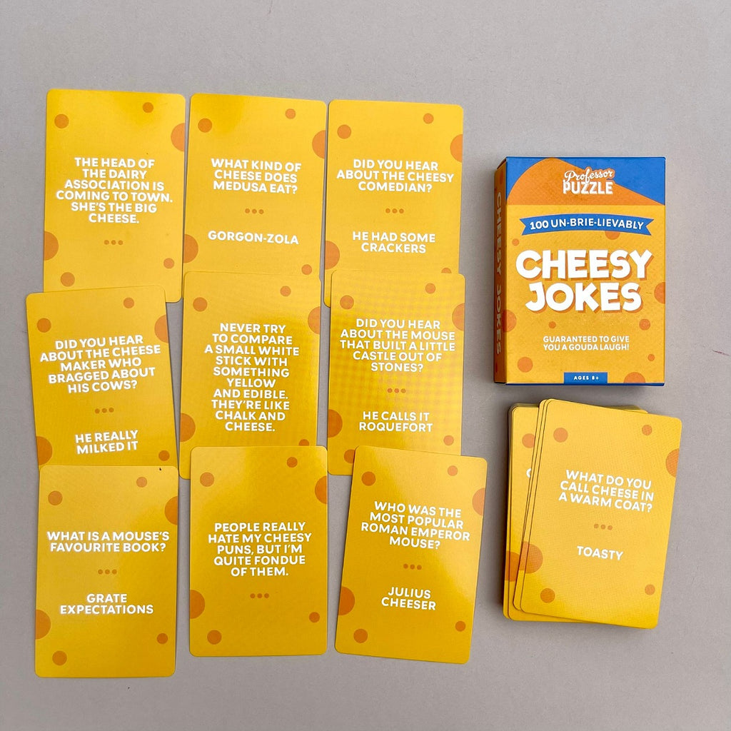 A box called 'Cheesy Jokes' by The Cheesy Puzzle, shown with several yellow joke cards and a small stack of cards on a light grey surface.