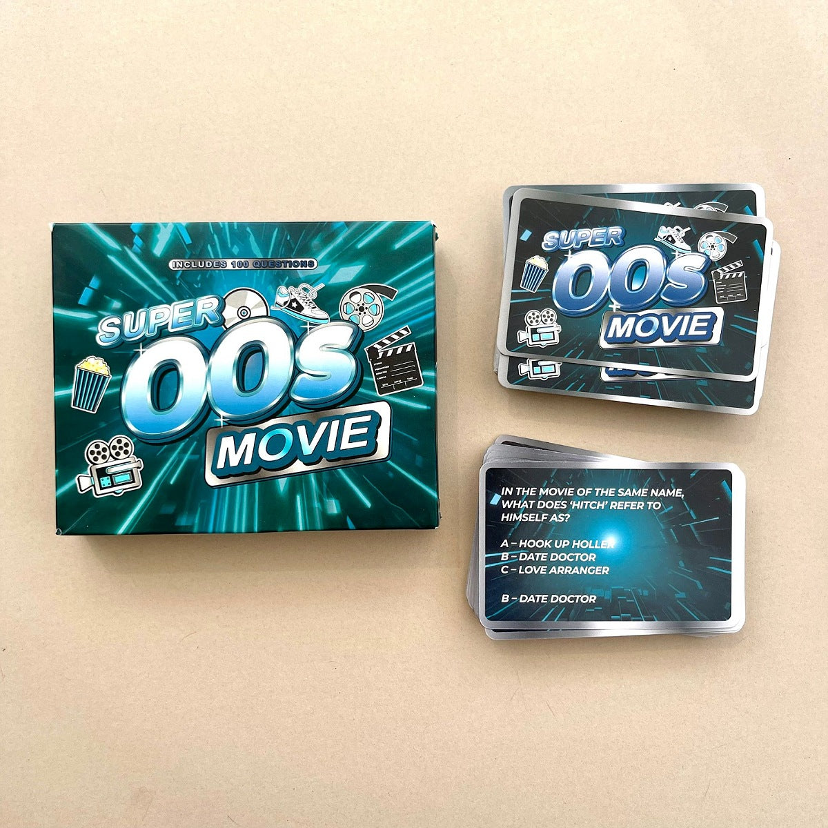 Super Oos Movie card game set with a teal and blue box, two stacks of cards, and one face-up card on a beige background.