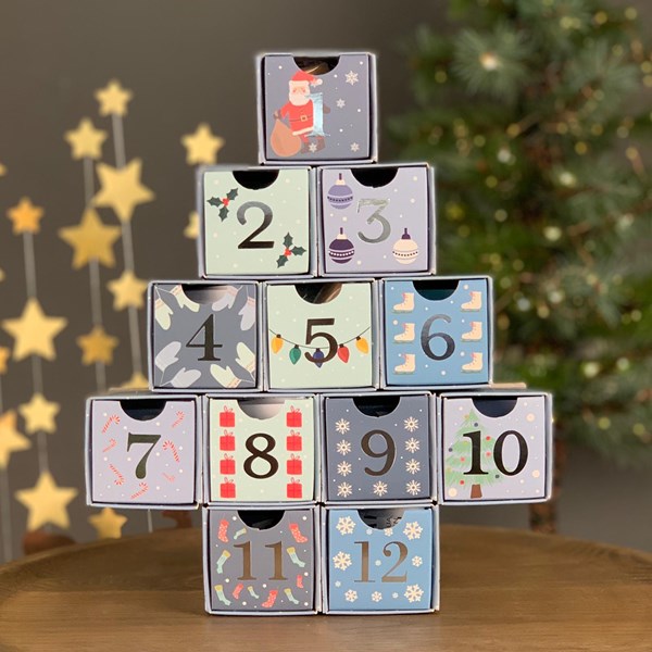 Stack of advent calendar boxes with numbers and Christmas-themed designs, against a festive background.