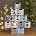 Stack of advent calendar boxes with numbers and Christmas-themed designs, against a festive background.