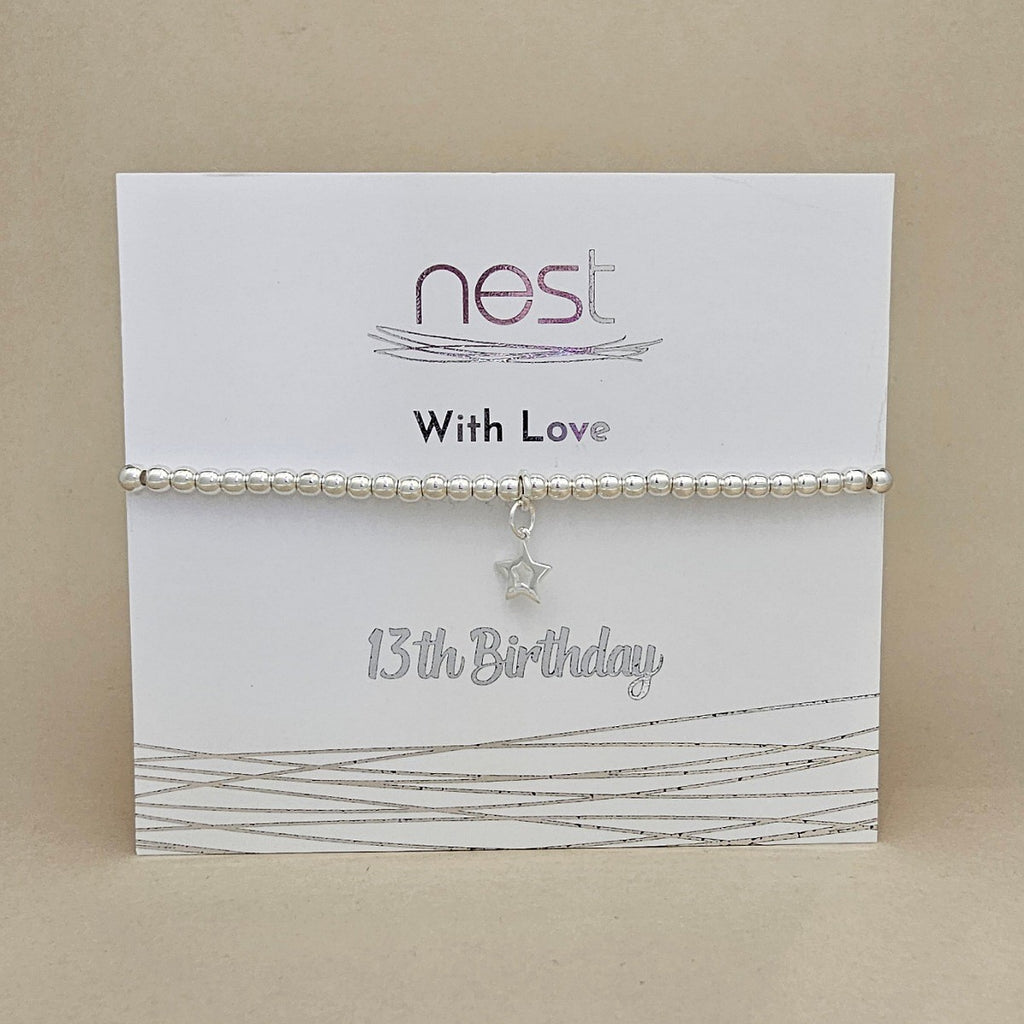 A silver beaded bracelet with a dangling star charm, presented on a white card labeled 'nest With Love 13th Birthday' against a beige background.
