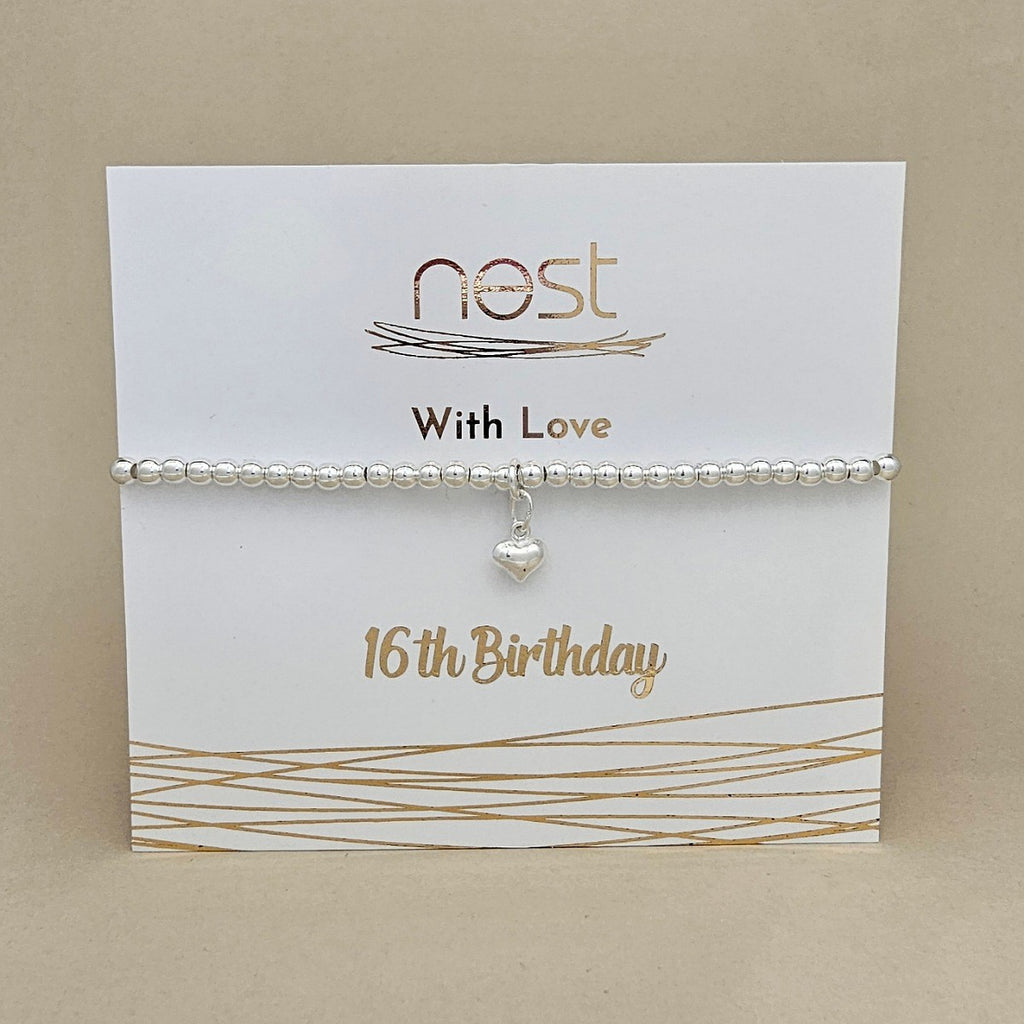 A silver beaded bracelet with a small heart charm, displayed on a white gift card printed with 'nest With Love 16th Birthday' against a beige background.