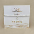 A silver beaded bracelet with a small heart charm, displayed on a white gift card printed with 'nest With Love 16th Birthday' against a beige background.