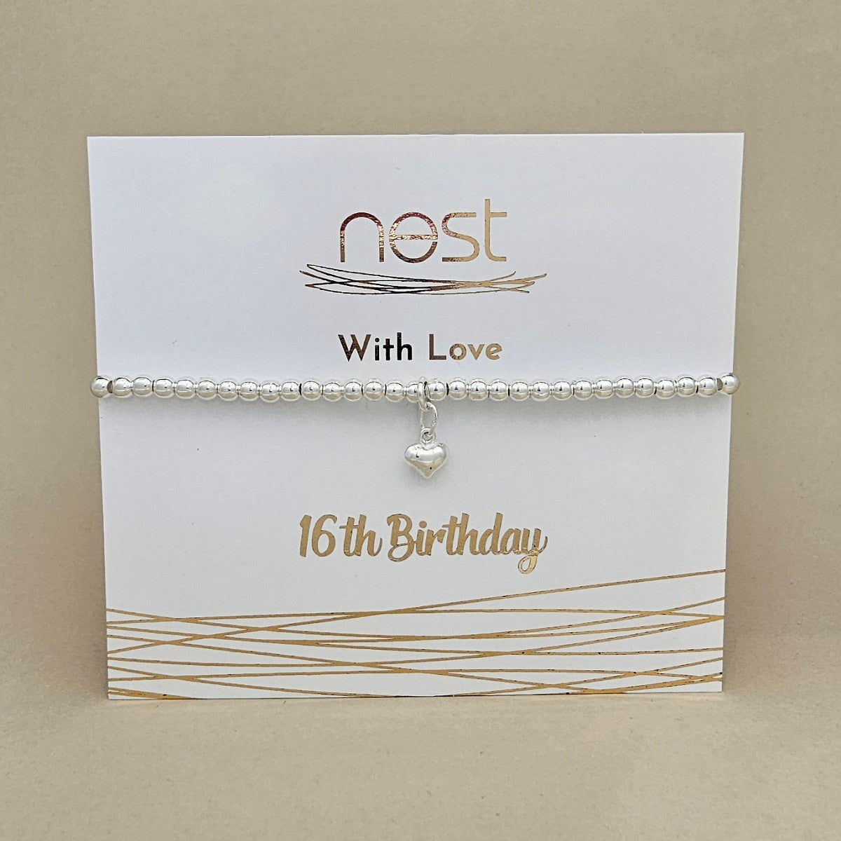 A silver beaded bracelet with a small heart charm, displayed on a white gift card printed with 'nest With Love 16th Birthday' against a beige background.