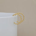 A gold hoop earrings with triangular sunburst details on the ends, displayed on a white cylindrical stand against a neutral beige background.