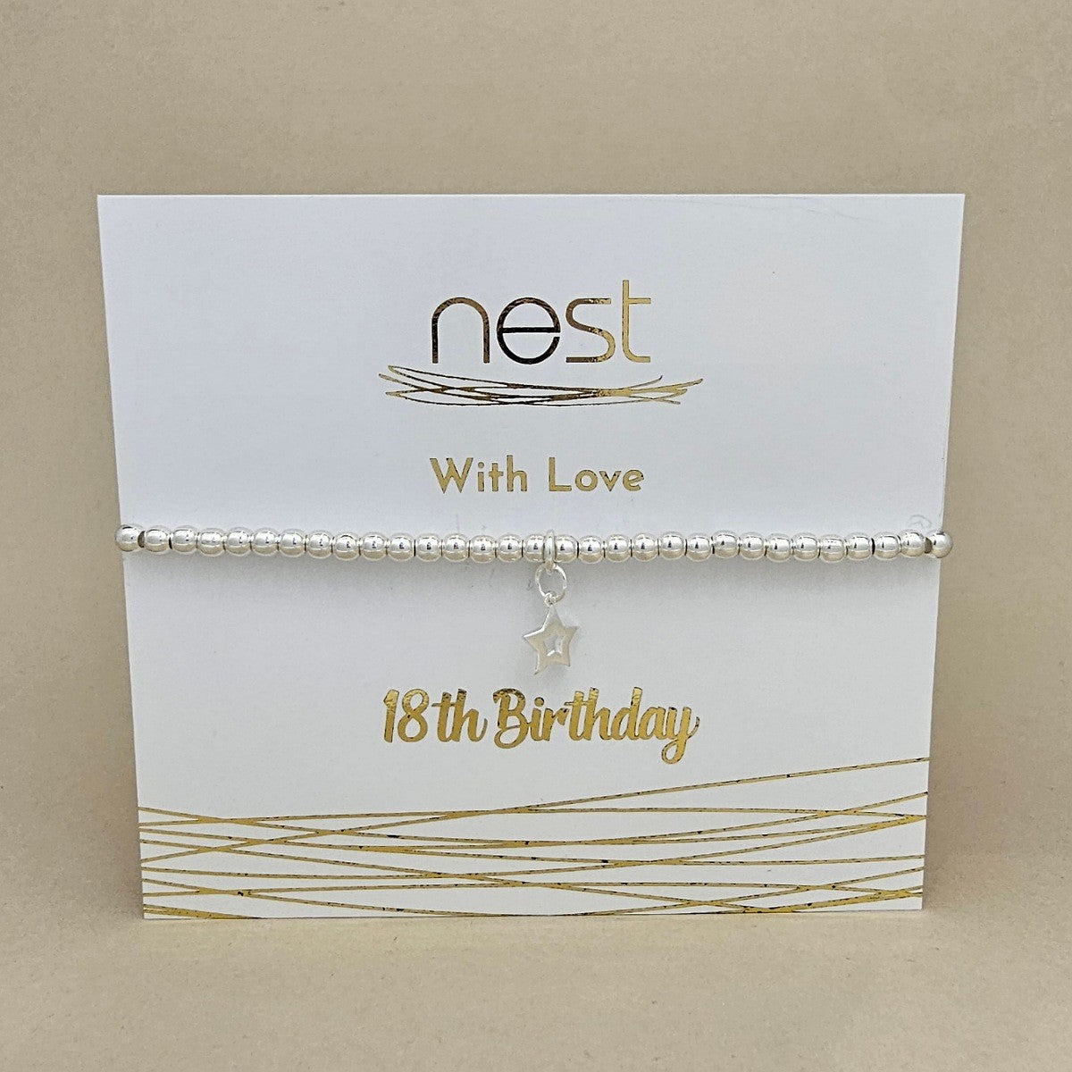 A silver beaded bracelet with a dangling star charm, presented on a white card with gold foil text reading 'nest With Love 18th Birthday' against a neutral beige background.