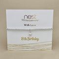 A silver beaded bracelet with a small dangling heart charm, displayed on a white card that reads 'nest With Love 18th Birthday' against a beige background.