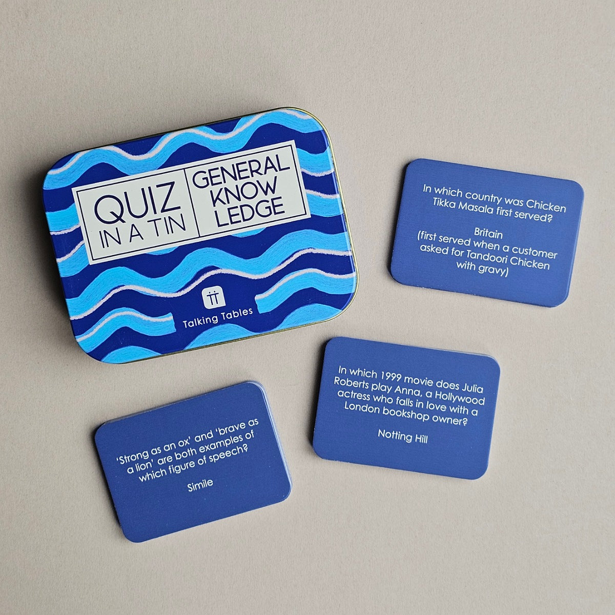 A set of blue and light blue trivia cards and a matching tin labeled 'Quiz in a Tin' and 'General Knowledge,' arranged on a neutral light grey background.