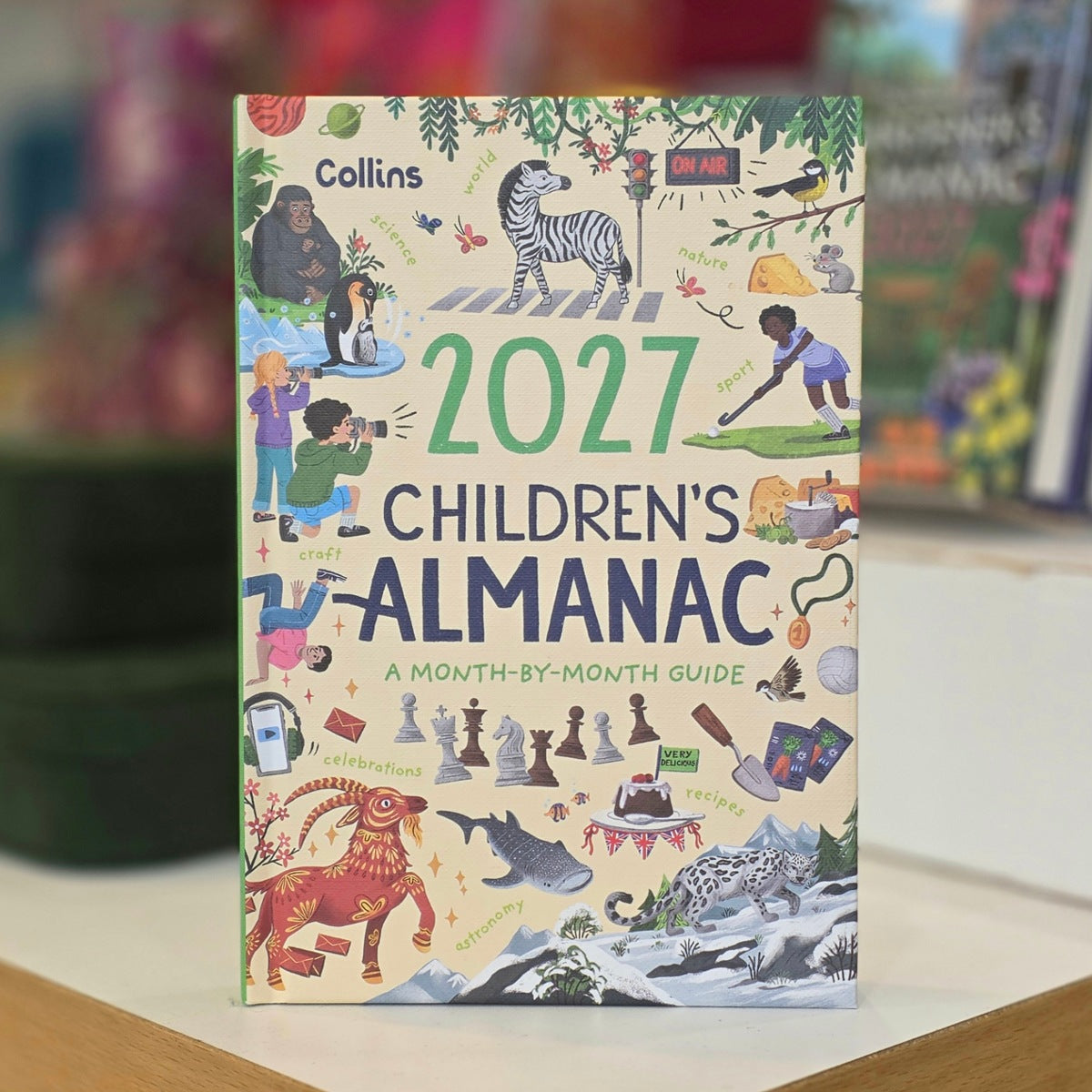 Collins 2027 Children's Almanac standing upright on a light surface with a blurred indoor background.