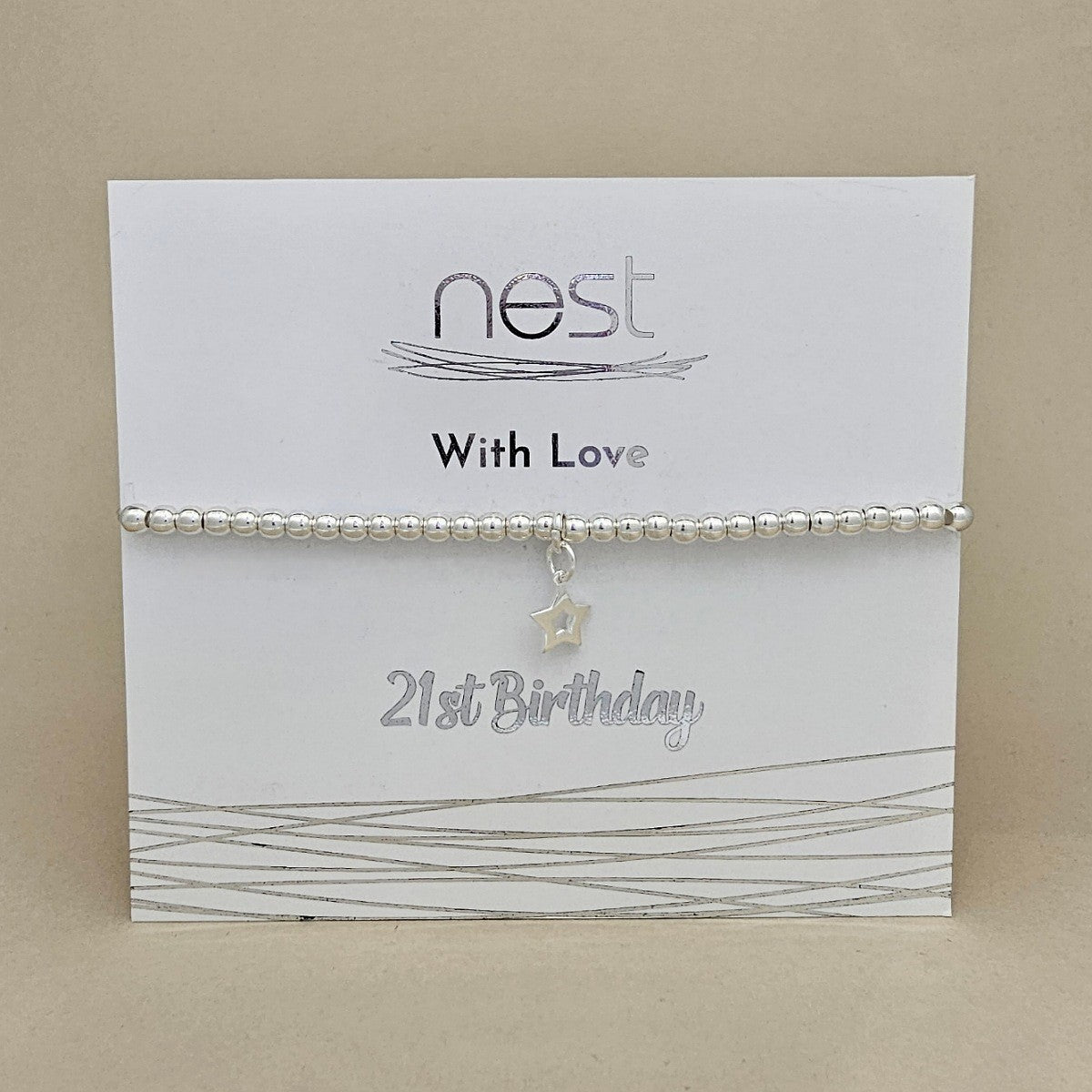 A silver beaded bracelet with a small star charm, presented on a white card labeled 'nest With Love 21st Birthday' against a beige background.
