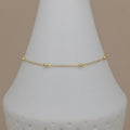 A delicate gold chain bracelet with three small bead accents, displayed on a white cone jewelry stand against a solid beige background.