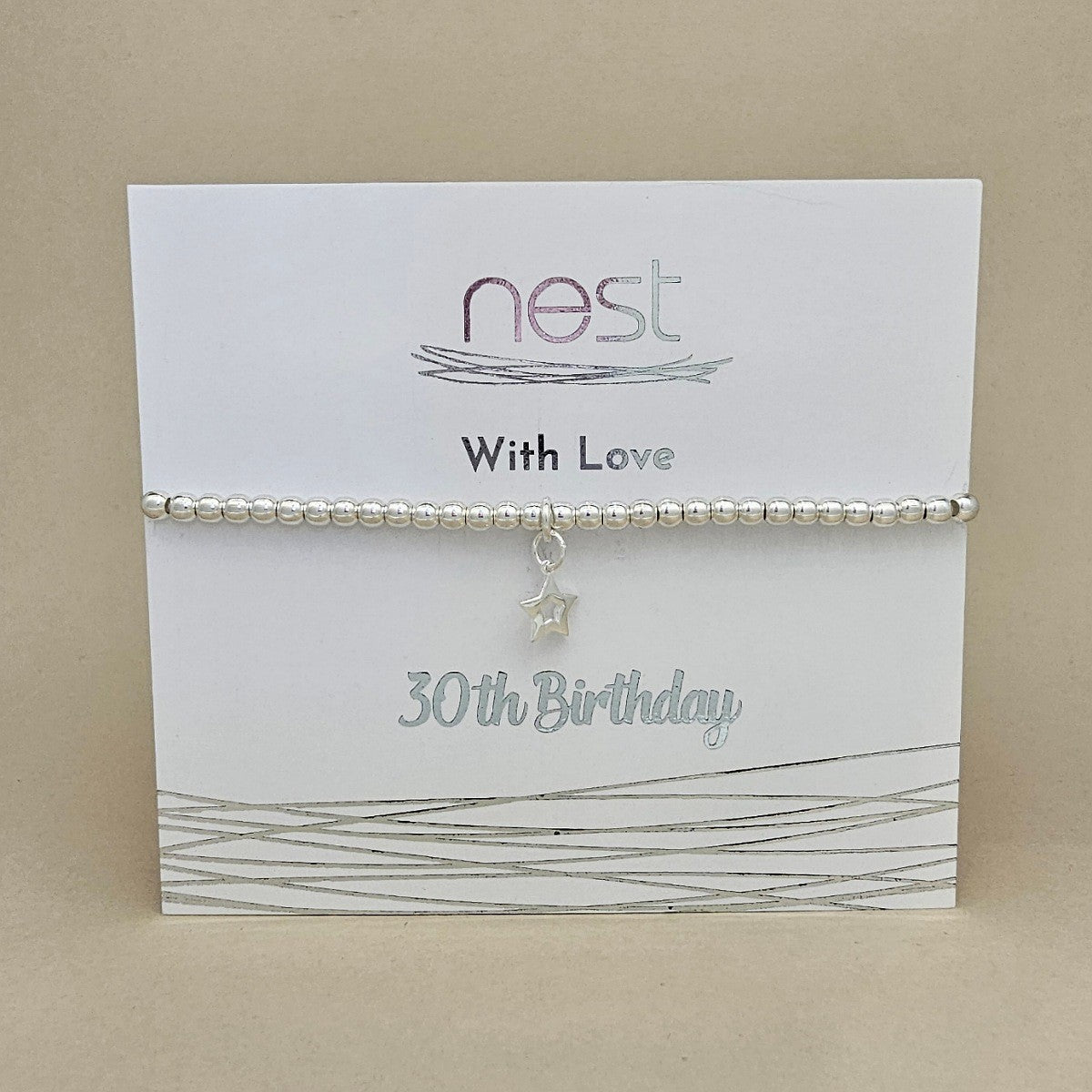 A silver beaded bracelet with a small dangling star charm, displayed on a white card labeled 'nest With Love 30th Birthday' against a beige background.