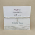A silver beaded bracelet with a small dangling heart charm, displayed on a white gift card that reads 'nest With Love 30th Birthday' against a beige background.