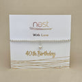 A silver beaded bracelet with a small heart charm, displayed on a white card printed with 'nest With Love 40th Birthday' in gold lettering, set against a neutral beige background.