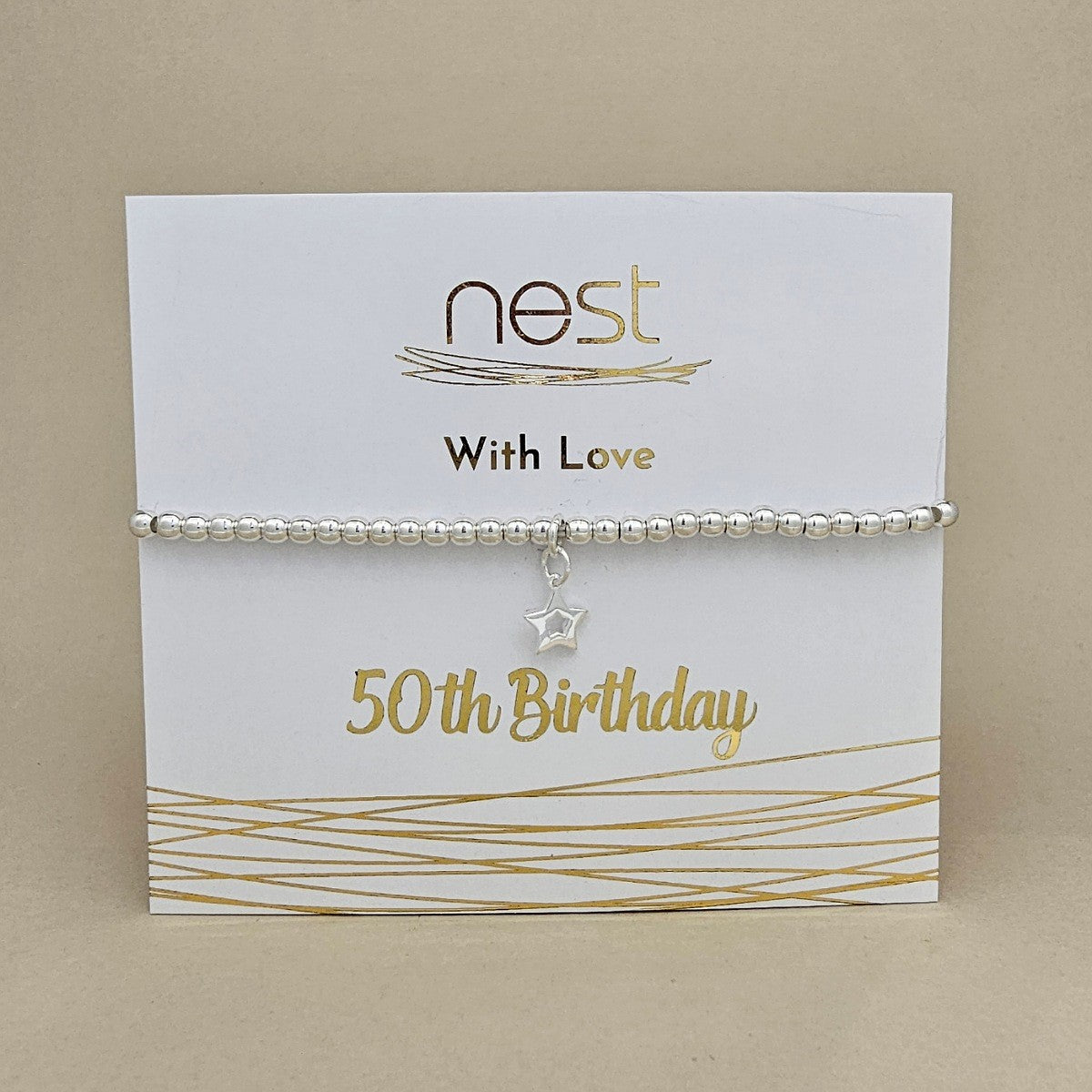 A silver beaded bracelet with a dangling star charm, presented on a white display card with gold foil text reading 'nest With Love 50th Birthday' against a beige background.