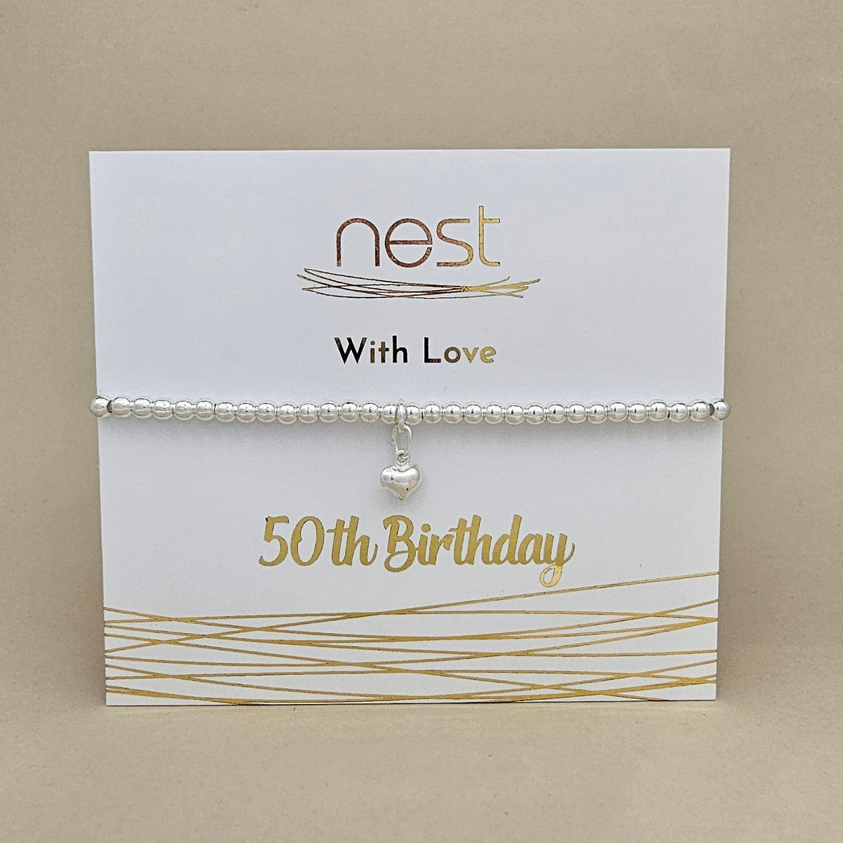 A silver beaded bracelet with a small heart charm displayed on a white card labeled 'nest With Love' and '50 th Birthday' against a beige background.