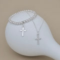 A silver beaded bracelet and a silver cross pendant necklace displayed on a white ceramic mannequin against a beige background.
