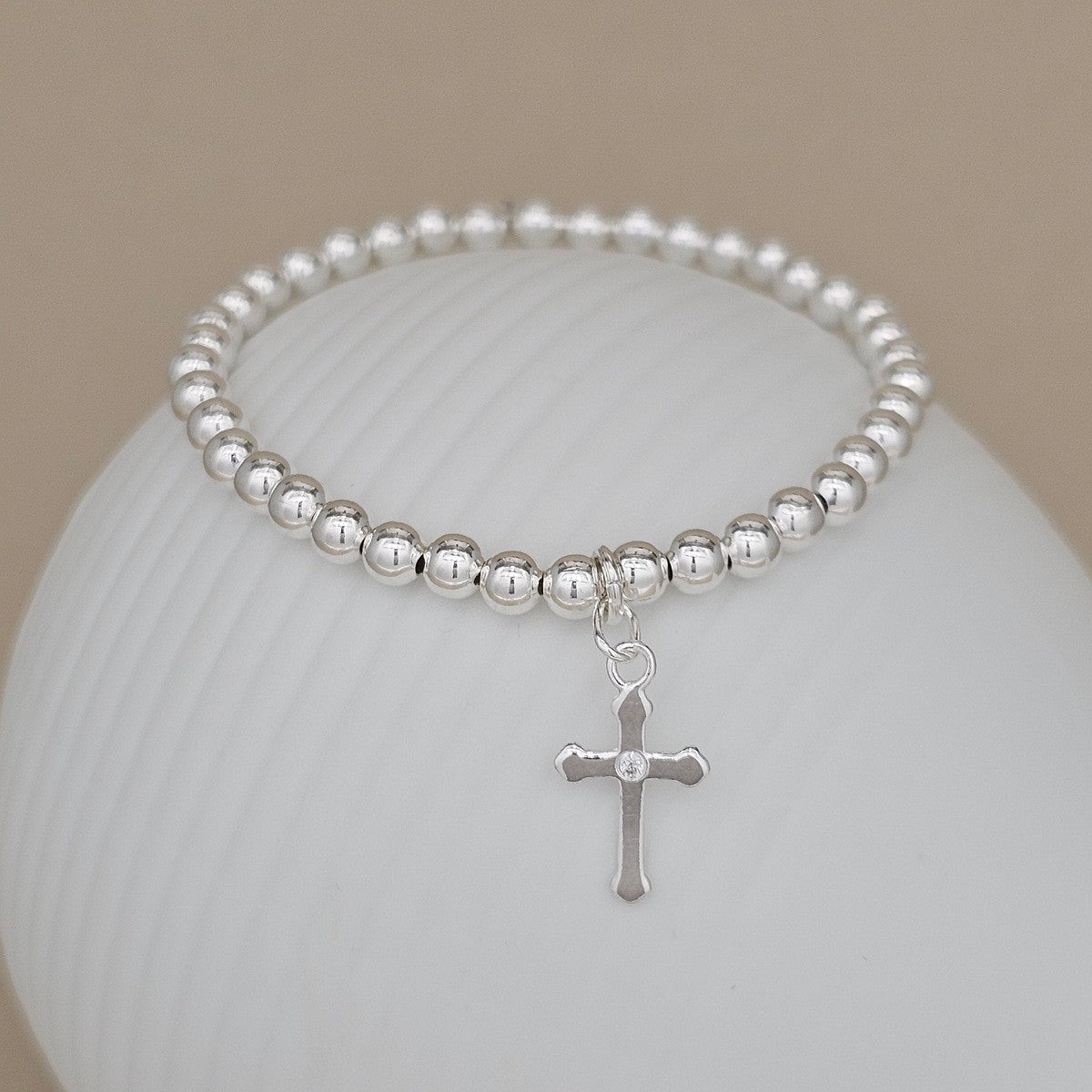 Silver beaded bracelet with a cross charm on a white surface