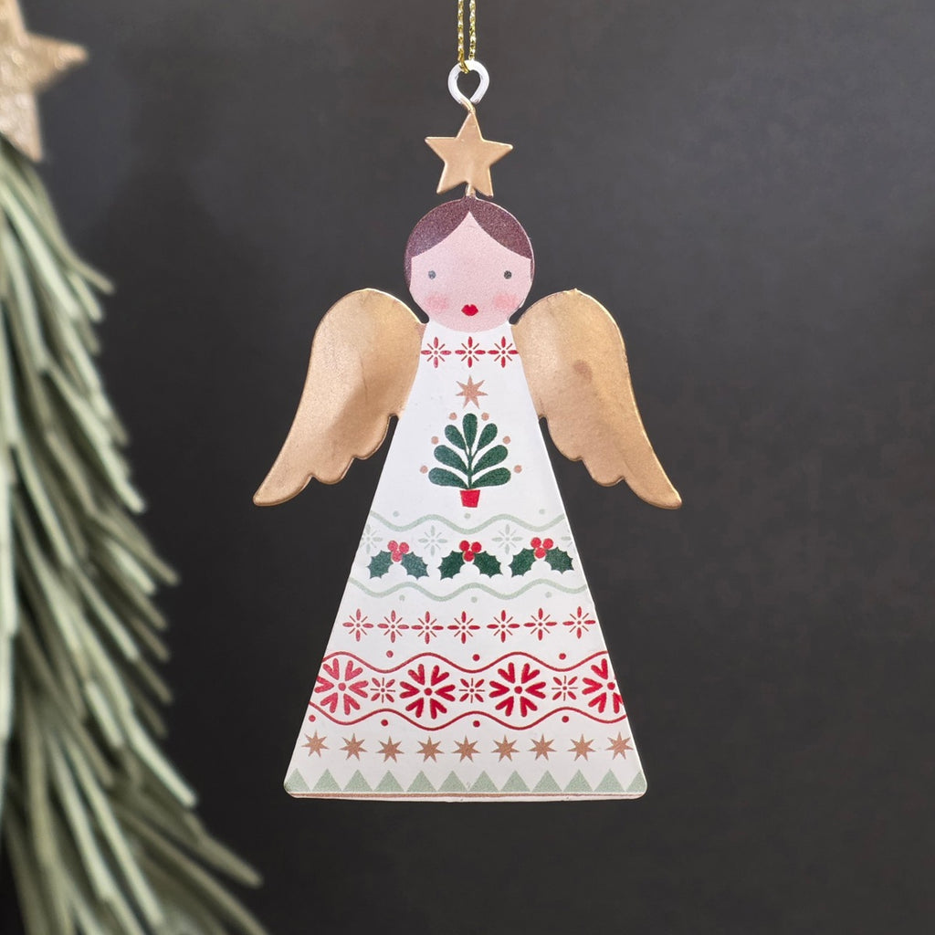 A decorative metal Christmas ornament shaped like an angel, featuring a cream-coloured body with hand-painted red, green, and gold holiday motifs and wings, hanging from a gold string against a dark background.