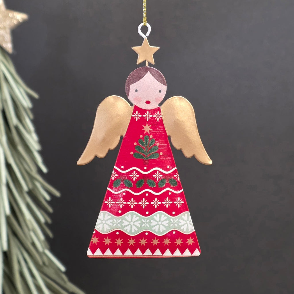 A decorative metal Christmas ornament shaped like an angel, featuring a red-coloured body with hand-painted red, green, and gold holiday motifs and wings, hanging from a gold string against a dark background.