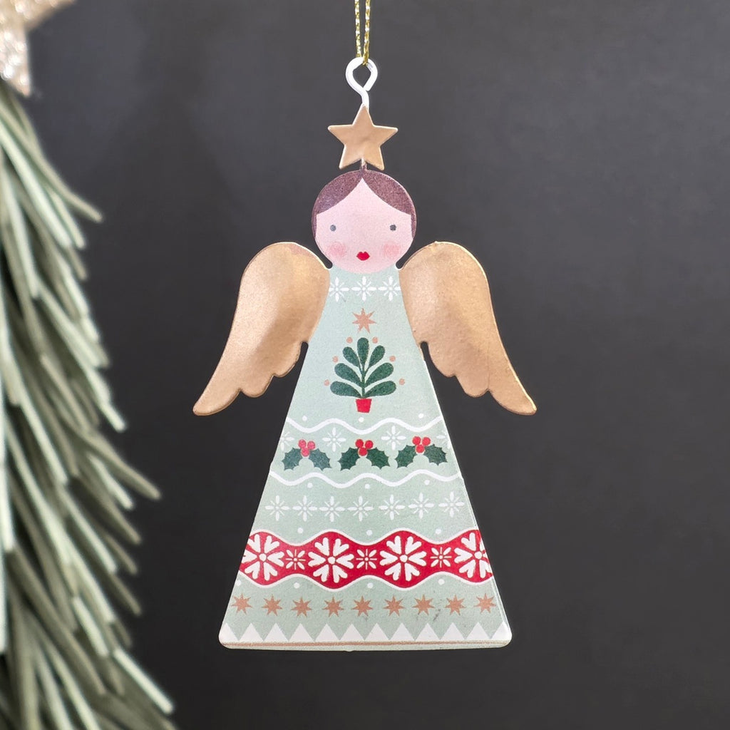 A decorative metal Christmas ornament shaped like an angel, featuring a light sage green-coloured body with hand-painted red, green, and gold holiday motifs and wings, hanging from a gold string against a dark background.