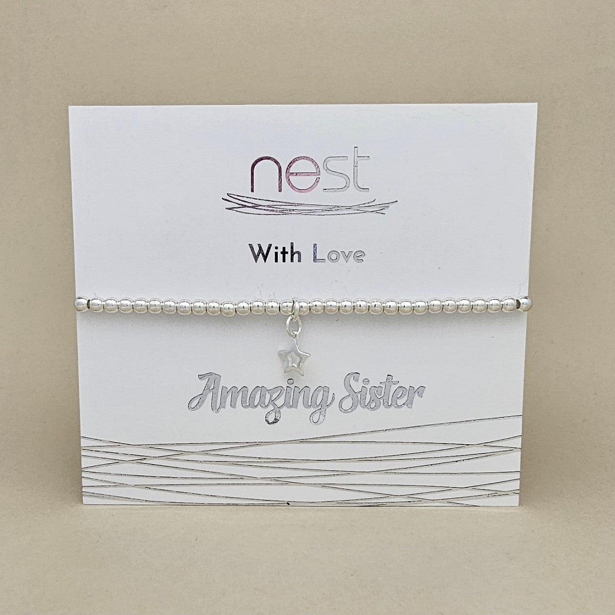 A silver beaded bracelet with a dangling star charm and small heart charm, displayed on a white card that reads 'nest With Love Amazing Sister' against a beige background.