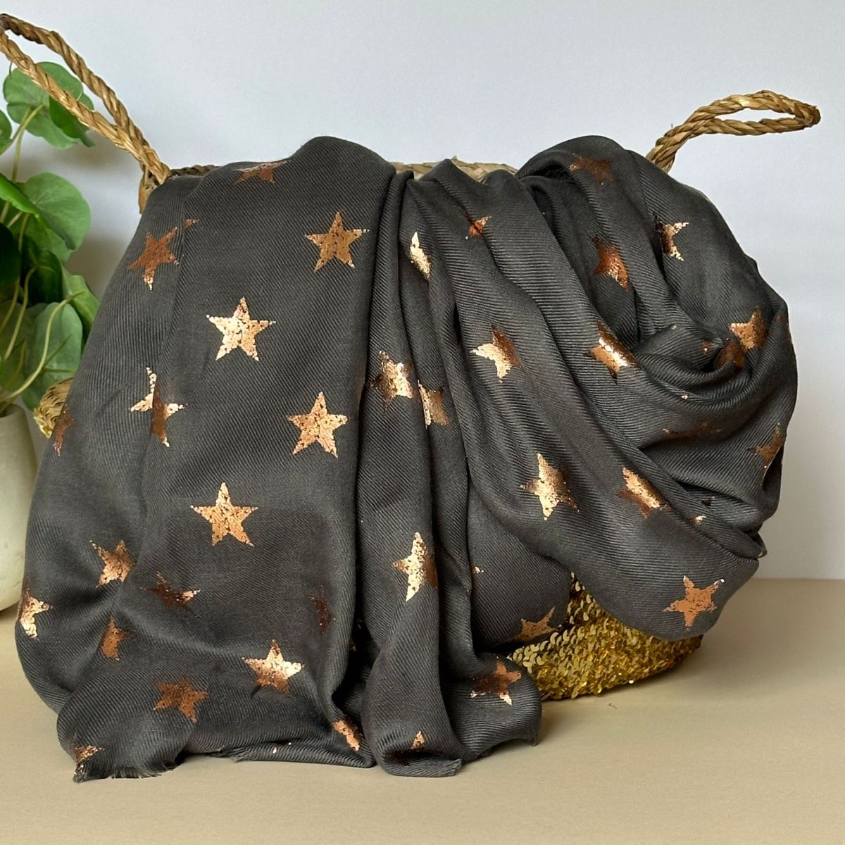 Charcoal grey scarf with repeating metalic antique gold star patterns draped over a woven basket on a light surface.