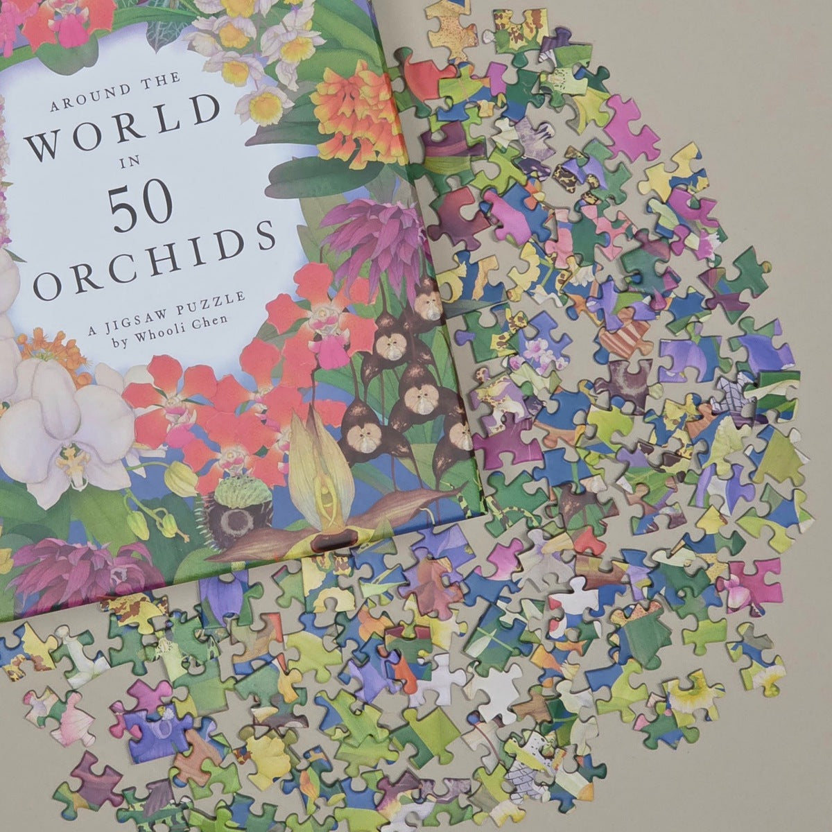 A jigsaw puzzle titled "Around the World in 50 Orchids" by WeiLi Chen, shown with many colorful puzzle pieces scattered around it on a light neutral background.