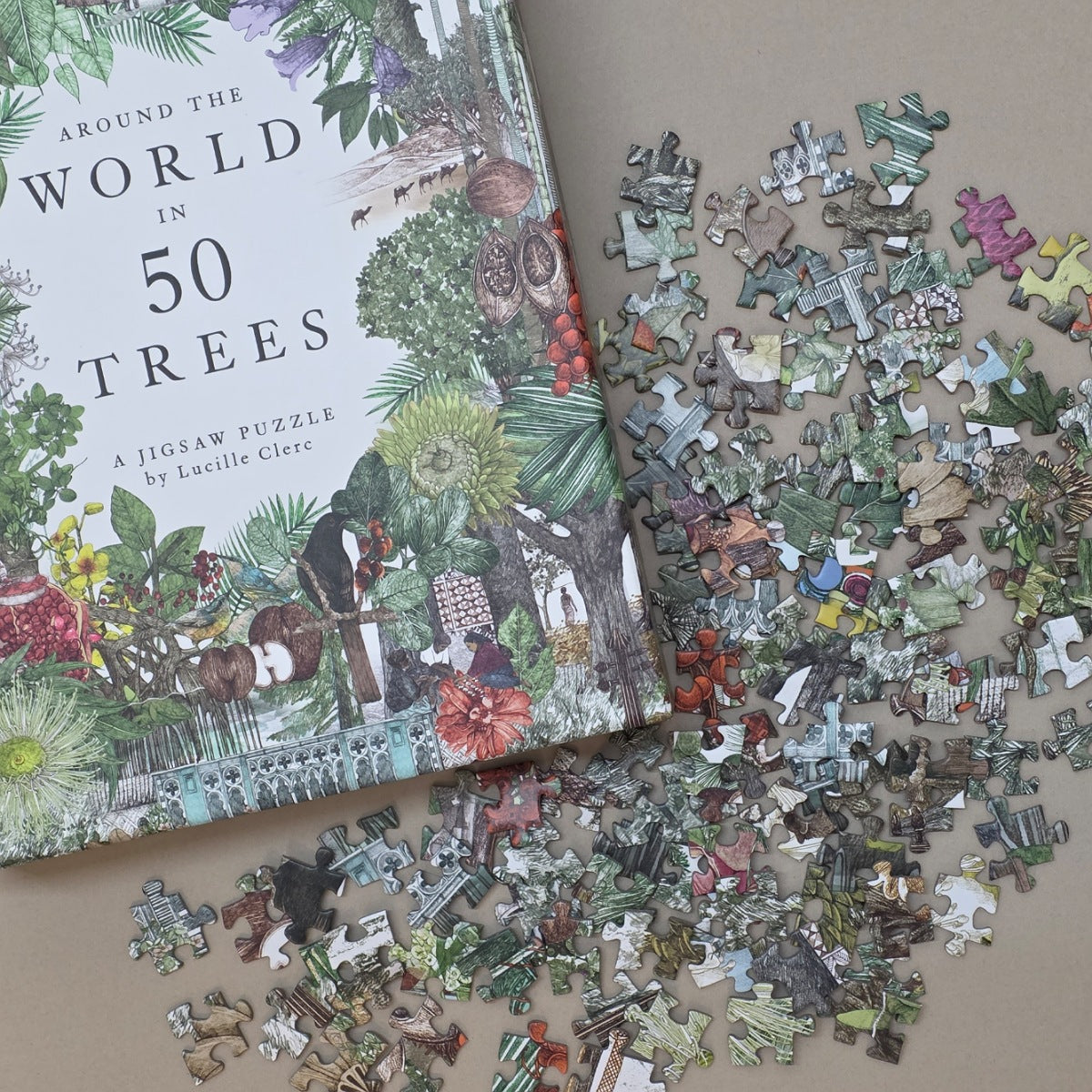 Jigsaw puzzle with pieces scattered on a surface, next to the packaging titled 'Around the World in 50 Trees'.