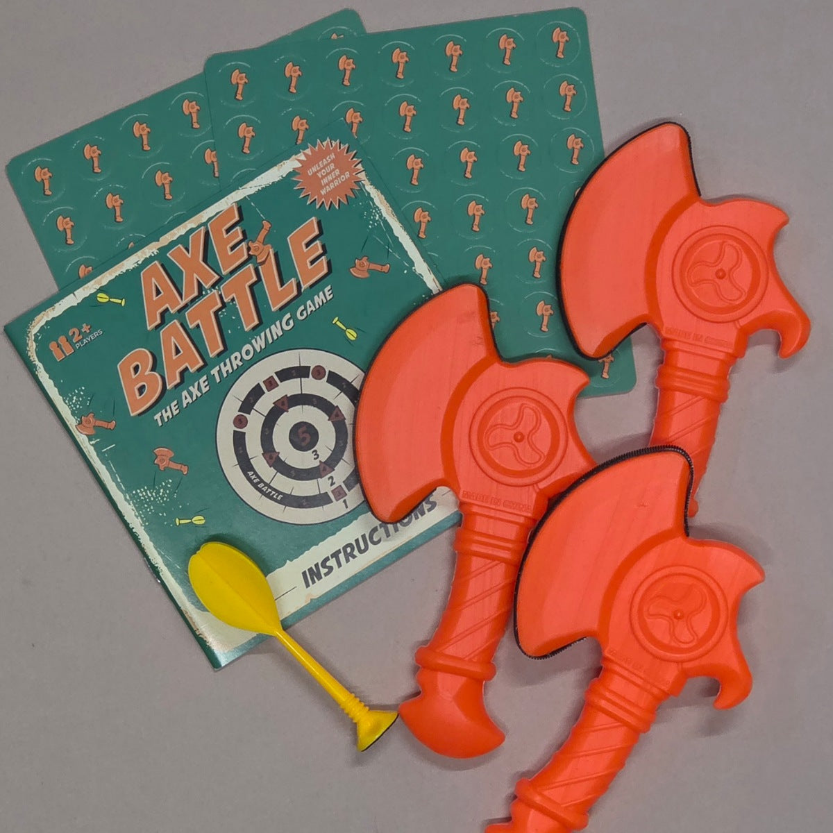 Axe Battle game set with three orange axes and a green instruction manual on a grey background