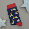 A single navy blue sock with a pattern of brown and white Jack Russell Terrier dogs, featuring red cuffs, heel and toe, displayed on a neutral grey background with white star-shaped props.