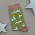 A single olive green sock with a pattern of brown and white Jack Russell Terrier dogs, featuring pink cuffs, heel and toe, displayed on a neutral grey background with white star-shaped props.