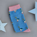 A single blue sock with various mallard duck silhouettes and pink yellow cuff, heel, and toe, laid flat on a light beige background with two white star decorations.