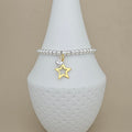 A silver beaded bracelet with a dangling gold star and silver heart charm, displayed on a white textured cone stand against a beige background.