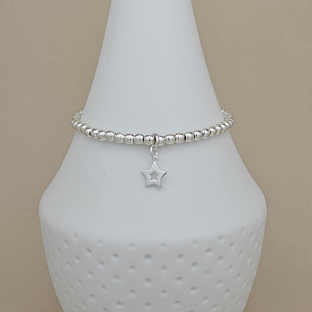 A silver beaded bracelet with a dangling star charm, displayed on a white ceramic jewelry bust against a beige background.