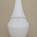 A silver beaded bracelet with a small dangling four-leaf clover charm, displayed on a white ceramic jewelry cone against a beige background.
