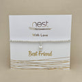 A silver beaded bracelet with a small dangling heart charm, displayed on a white card that reads 'nest With Love Best Friend' with gold decorative lines, set against a beige background.