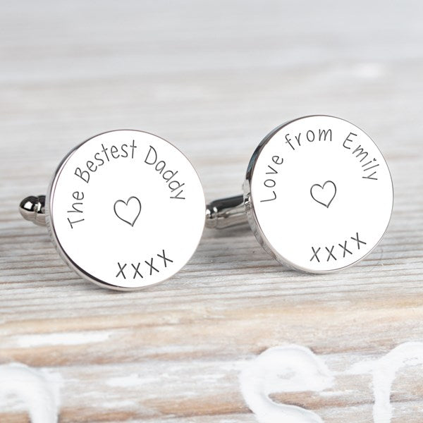 A pair of round silver cufflinks engraved with personalised messages and heart designs, with the text 'The Bestest Daddy xxx' and Love from Emily xxx' displayed on a light wood background.