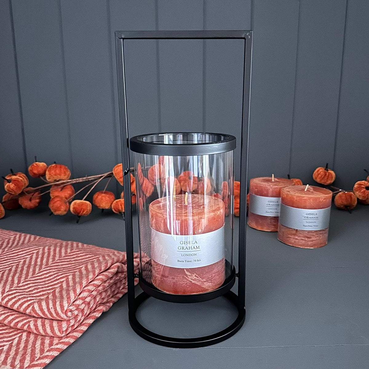 Decorative black metal lantern holder on a grey surface with pumpkins and a red patterned cloth.