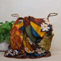 A multicolor patterned scarf draped over a woven basket with rope handles, set against a plain light background with a green potted plant on the left.