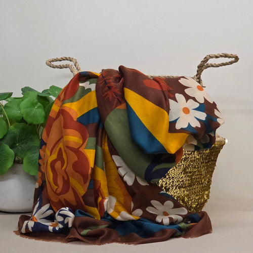 A multicolor patterned scarf draped over a woven basket with rope handles, set against a plain light background with a green potted plant on the left.