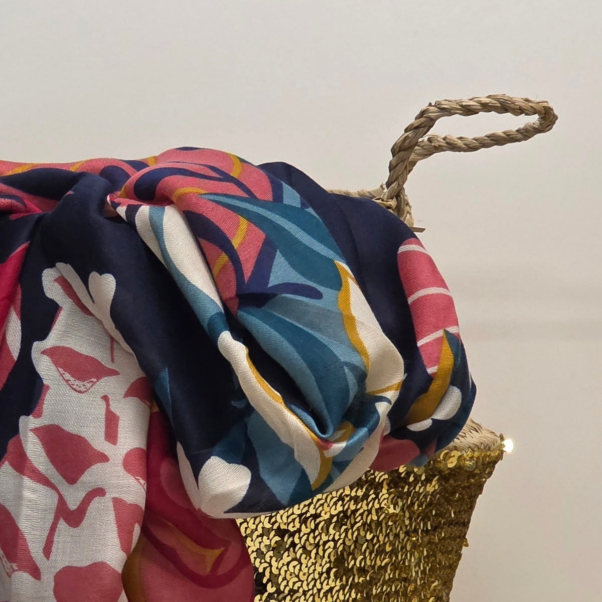 A multicolor tropical print scarf draped over a woven gold chair, featuring navy blue, pink, teal, yellow, and white patterns.