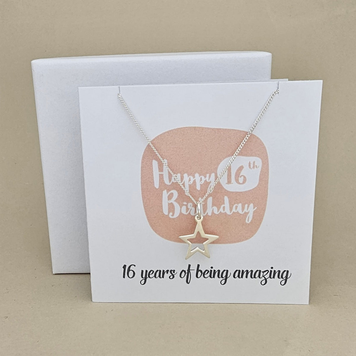 A silver open star necklace displayed on a white card with a peach rounded square and the text 'Happy 16th Birthday' and ’16 years of being amazing,' 
