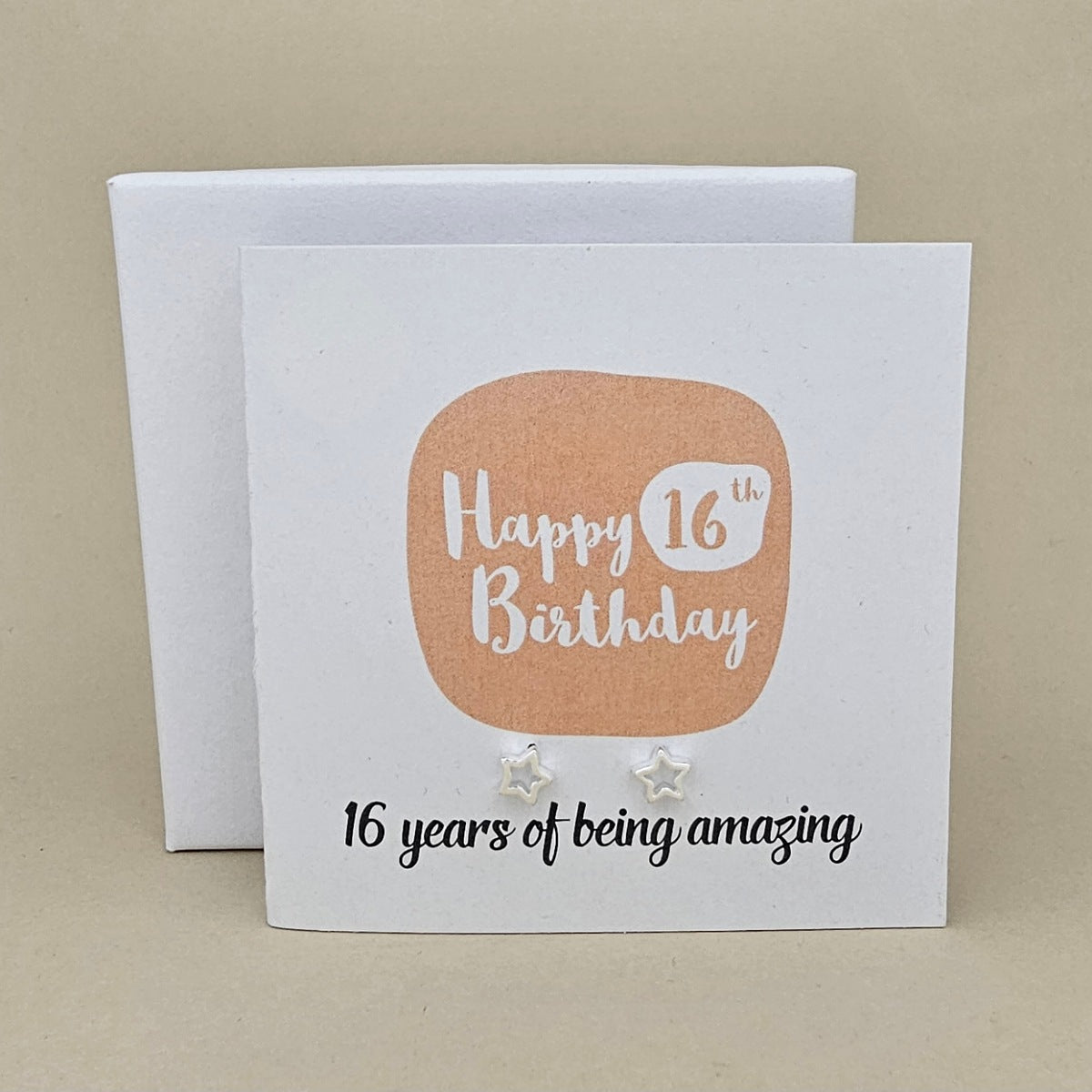 A pair of silver open star earrings displayed on a white card with a peach rounded square and the text 'Happy 16th Birthday' and ’16 years of being amazing,' 

