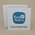 A pair of silver open star earrings displayed on a white card with a blue rounded square and the text 'Happy 18th Birthday' and ’18 years of being amazing,' 
