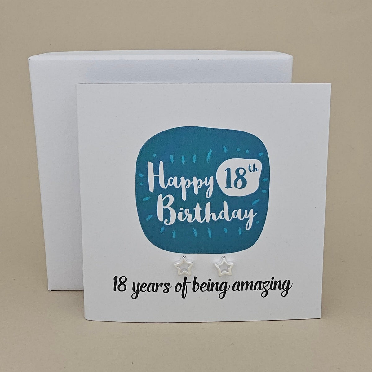 A pair of silver open star earrings displayed on a white card with a blue rounded square and the text 'Happy 18th Birthday' and ’18 years of being amazing,' 
