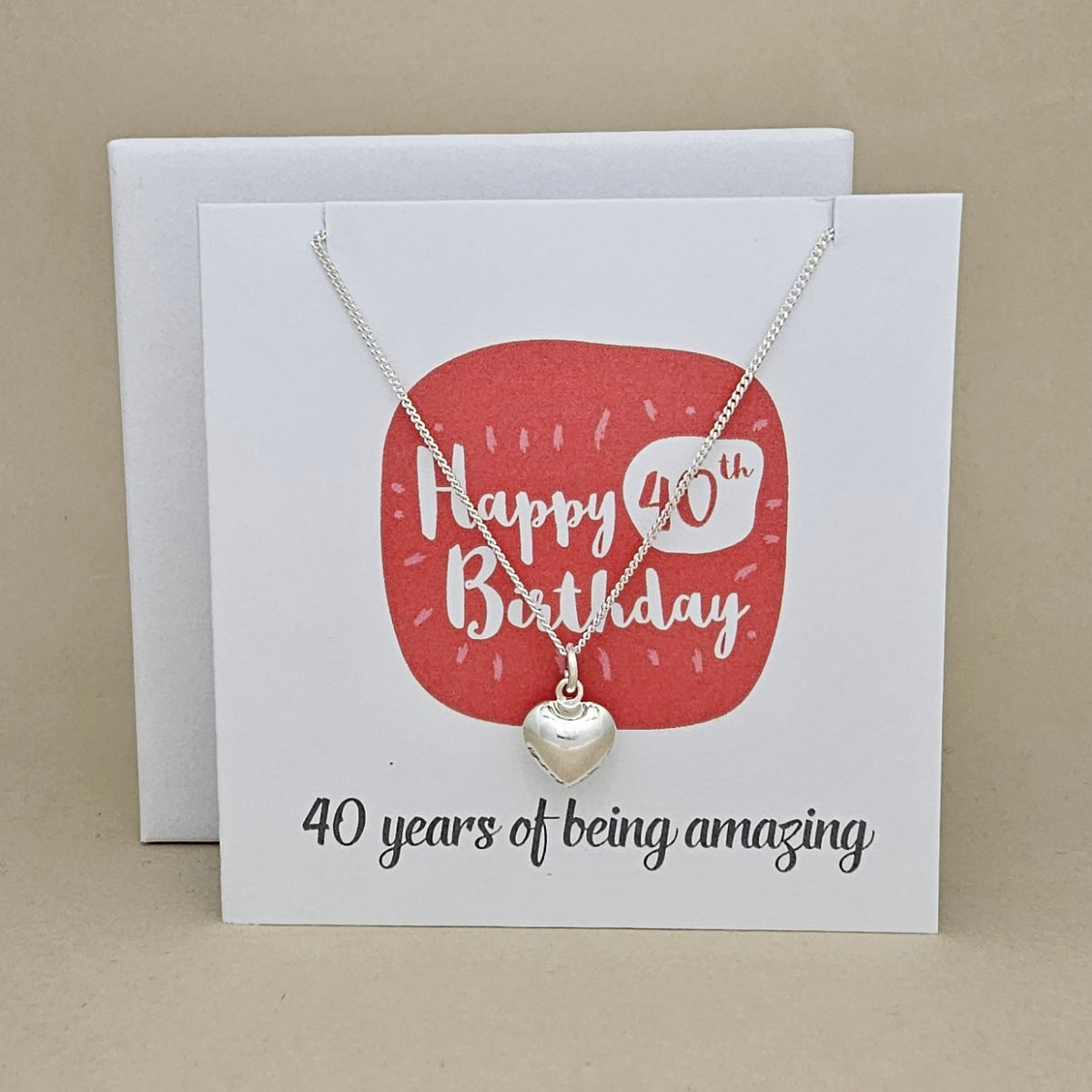 A silver heart necklace displayed on a white card with a red rounded square and the text 'Happy 40th Birthday' and ’40 years of being amazing,'
