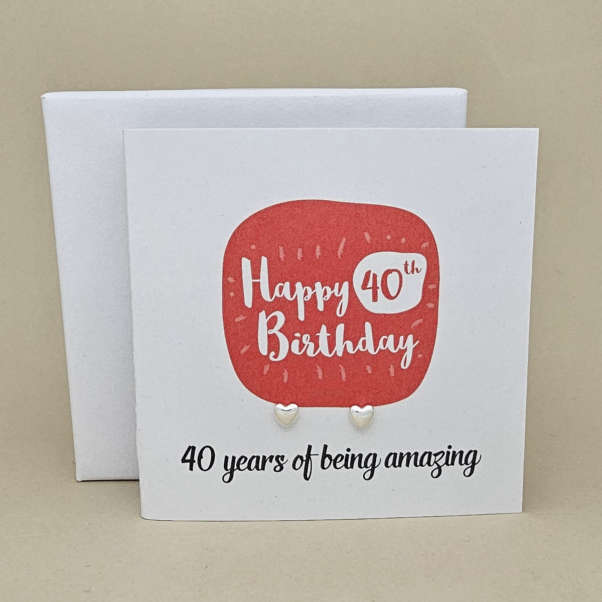 A pair of silver heart earrings displayed on a white card with a red rounded square and the text 'Happy 40th Birthday' and ’40 years of being amazing,'
