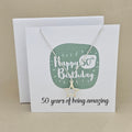 A silver open star necklace displayed on a white card with a green rounded square and the text 'Happy 50th Birthday' and ’50 years of being amazing,'
