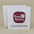 A pair of silver open star earrings displayed on a white card with a burgundy rounded square and the text 'Happy 60th Birthday' and '60 years of being amazing,'.